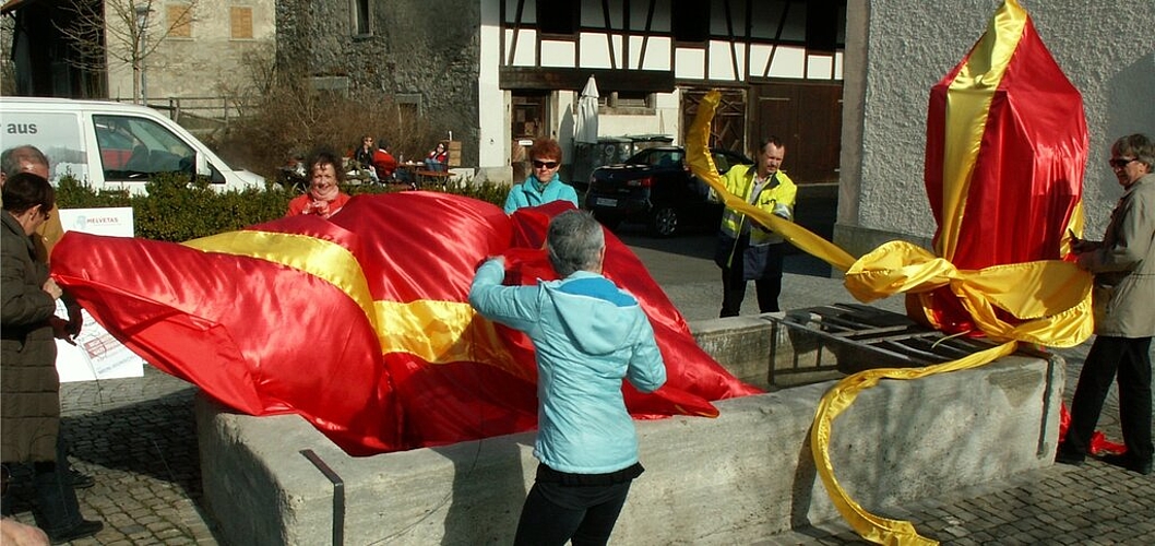 Mitarbeiterinnen und Mitarbeiter von Helvetas und Gemeinde enthüllen den verpackten Pöschtlibrunnen. Fotos: ska
