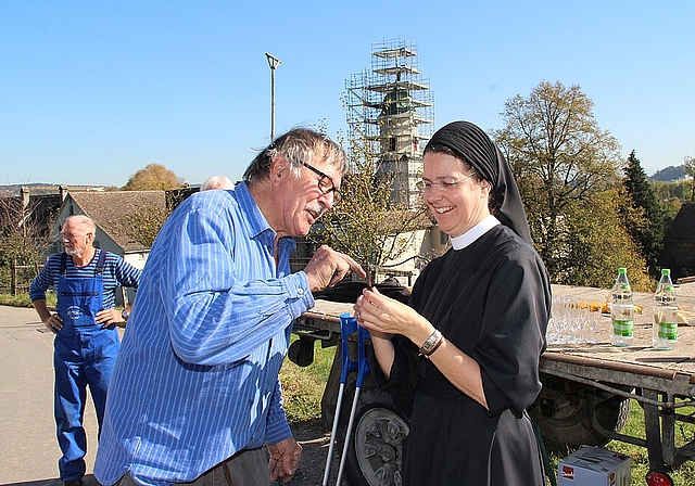 Metallbauer Ueli Schneider übergibt Priorin Irene einen Brieföffner, damit sie künftig Dokumente aus der Turmkugel besser öffnen kann. Im Hintergrund der Kirchenturm mit dem restaurierten Kreuz samt Kugel.